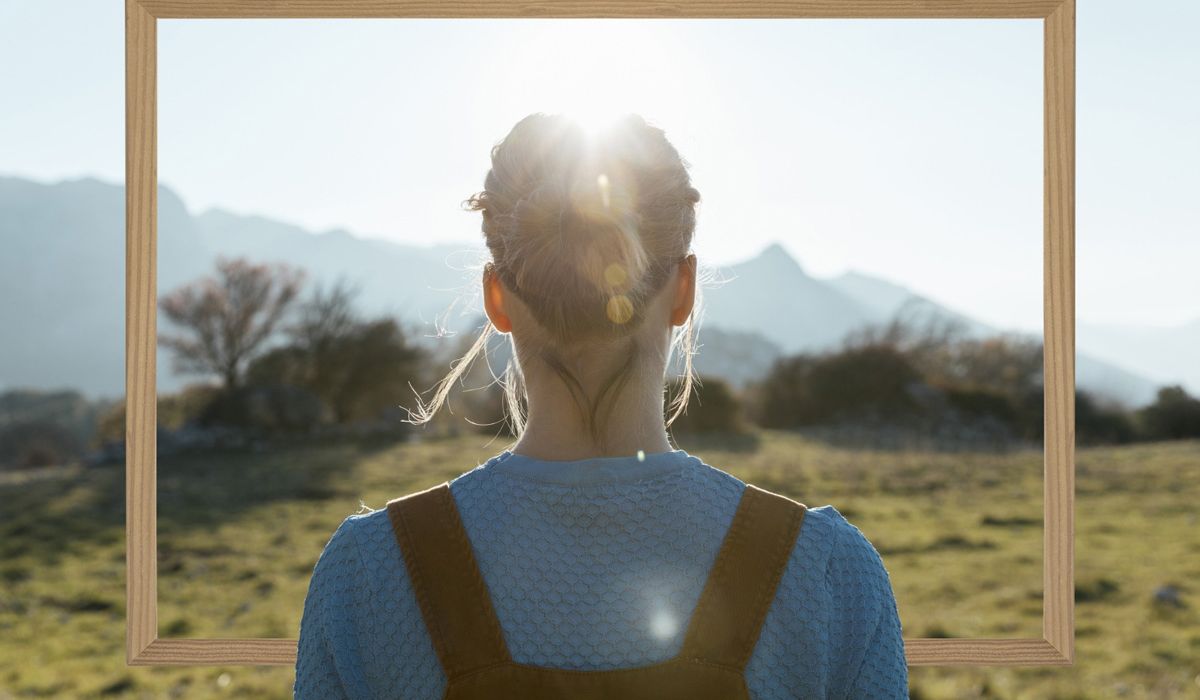 A woman gazes at the sun through a rectangular frame, highlighting her silhouette against a bright sky.